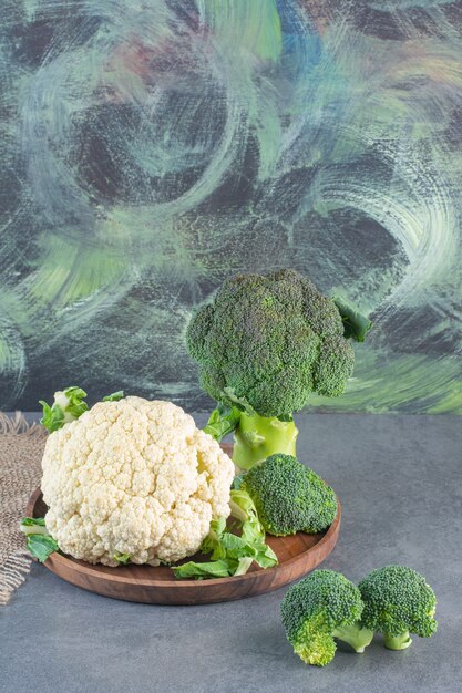 Wooden plate of fresh green broccoli and cauliflowers on stone surface