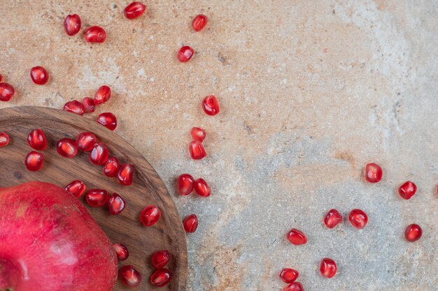 Wooden plate of fresh juicy pomegranate seeds on marble surface.