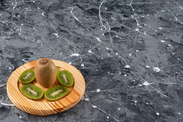 Wooden plate of fresh kiwi slices on marble background.