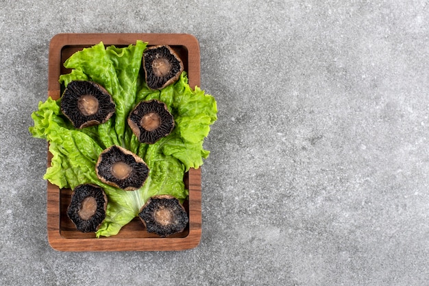 Wooden plate of fried mushrooms with lettuce on stone table.