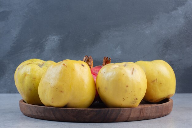 Wooden plate full of apple quince on grey background.