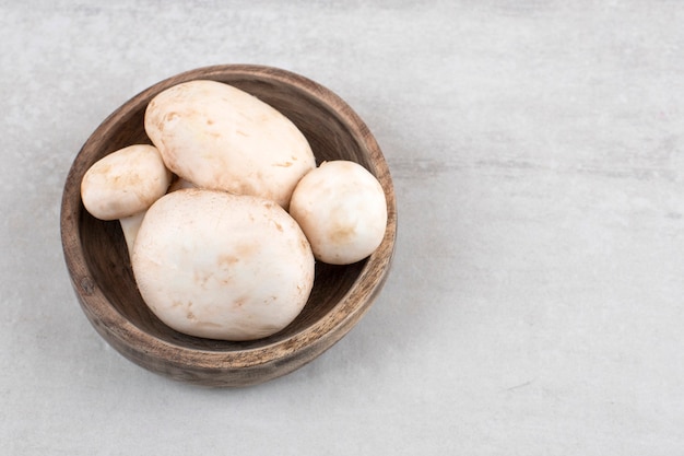 A wooden plate full of fresh champignon mushrooms placed on a stone table. 