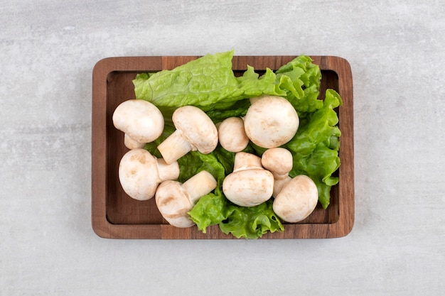 A wooden plate full of fresh champignon mushrooms placed on a stone table. 