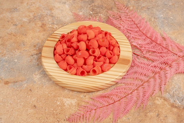 A wooden plate full of red unprepared macaroni . High quality photo