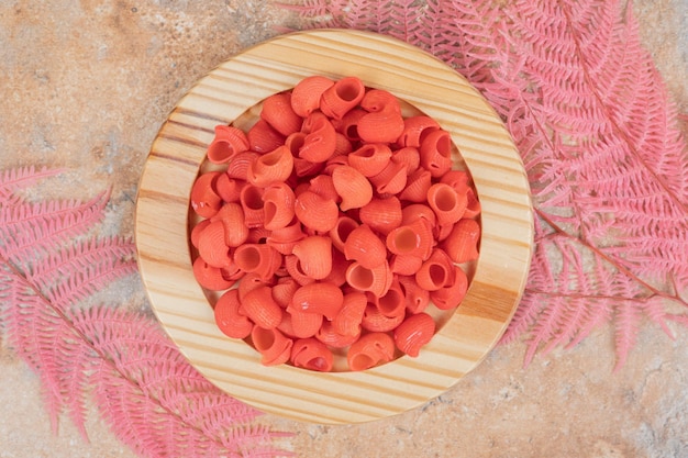 A wooden plate full of red unprepared macaroni . 