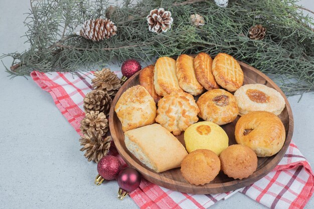 A wooden plate full of sweet pastries with Christmas balls and pinecones