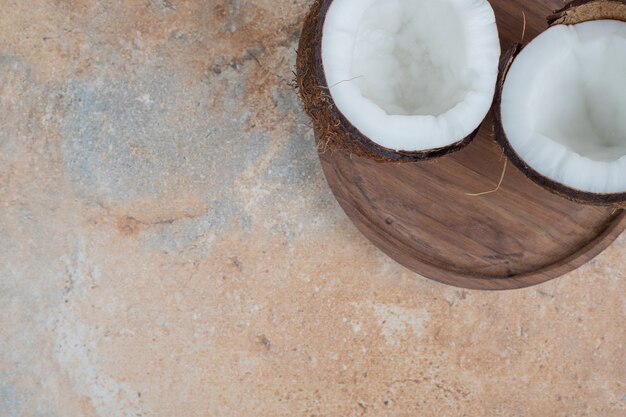 Wooden plate of half cut ripe coconuts on marble surface.