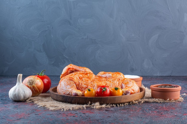 Piatto di legno di pollo intero marinato sulla superficie di marmo