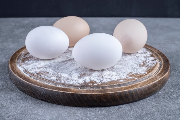 무료 사진 밀가루와 흰색과 갈색 닭고기 달걀의 나무 접시는 돌 테이블에 배치합니다.
