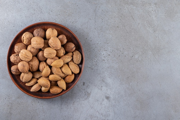 Wooden plate of organic shelled walnuts and almonds on stone background. 