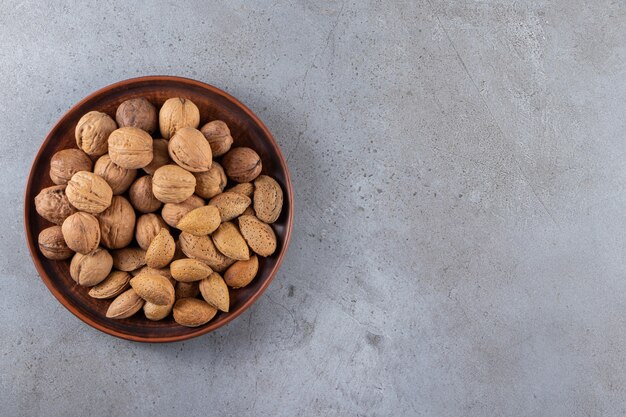 Деревянная тарелка из органических очищенных грецких орехов и миндаля на каменном фоне.