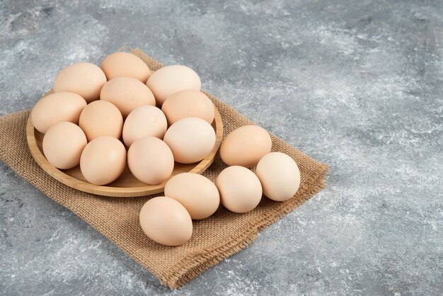 Wooden plate of organic uncooked eggs on marble surface.