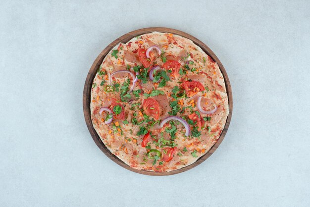 A wooden plate of pita bread with sliced tomato and onion.