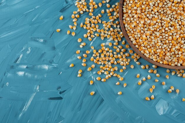 Wooden plate of raw corn kernels on blue surface.