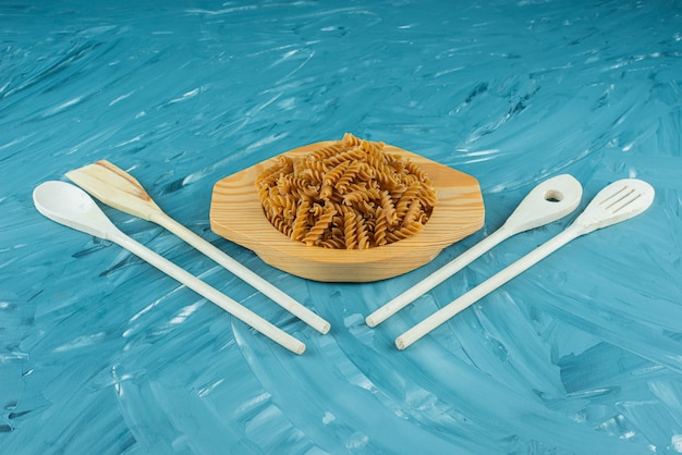Free photo wooden plate of raw dry fusilli on marble surface.