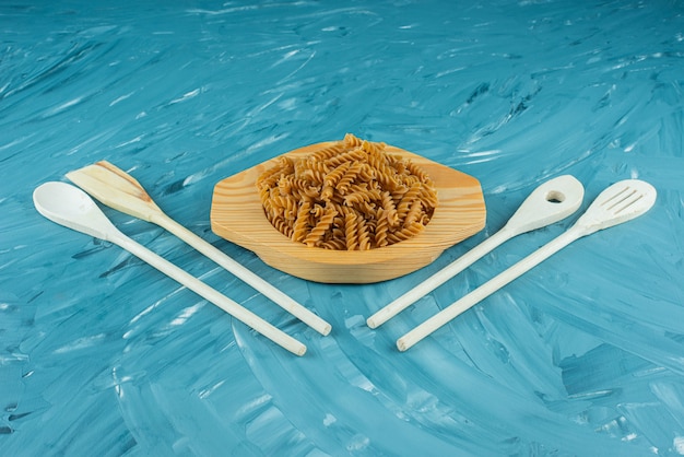 Wooden plate of raw dry fusilli on marble surface. 