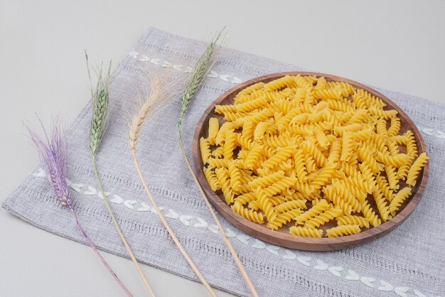 Foto gratuita piatto di legno di pasta cruda sulla tovaglia con grano colorato.
