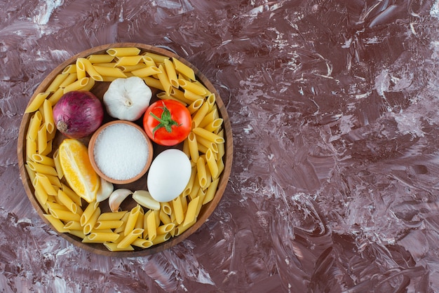 Foto gratuita piatto di legno di penne crude e verdure sulla superficie in marmo.