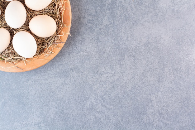 Wooden plate of raw white eggs on stone table.