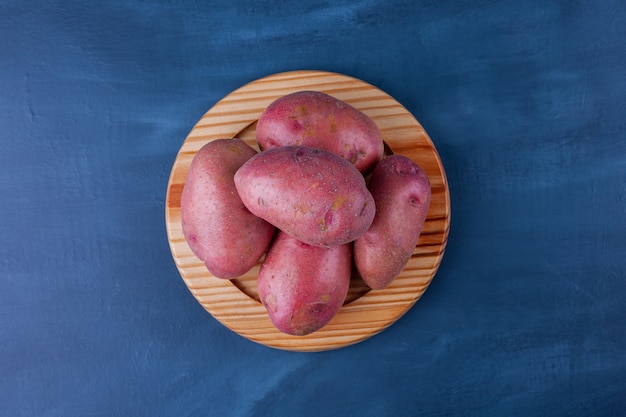Wooden plate of ripe sweet potatoes on blue surface.