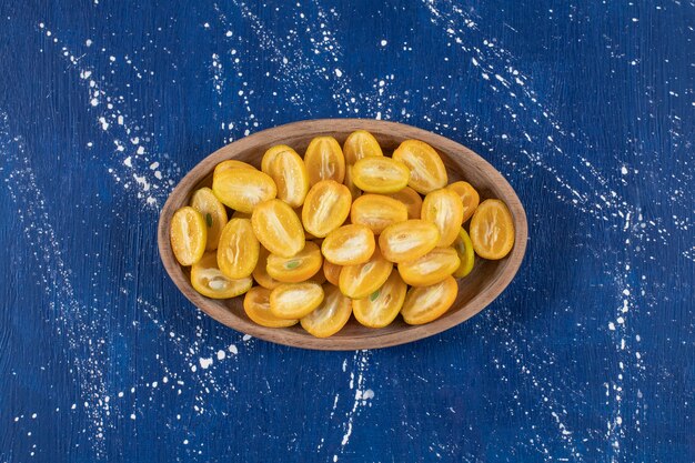 Wooden plate of sliced kumquat fruits on marble surface