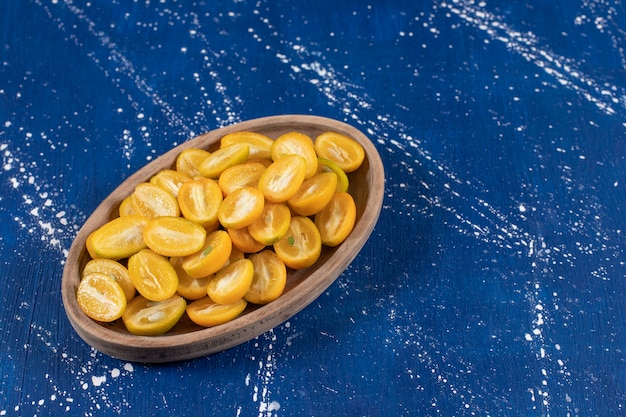 Free photo wooden plate of sliced kumquat fruits on marble surface