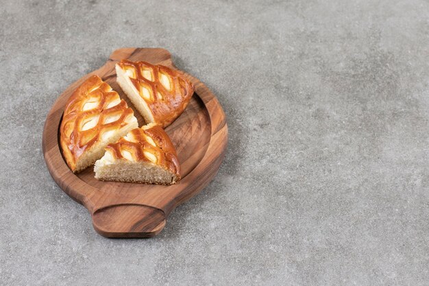 Деревянная тарелка нарезанного вкусного пирога на мраморной поверхности.