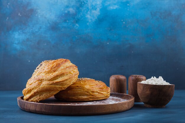 Wooden plate of sweet pastries with seeds on blue surface. 