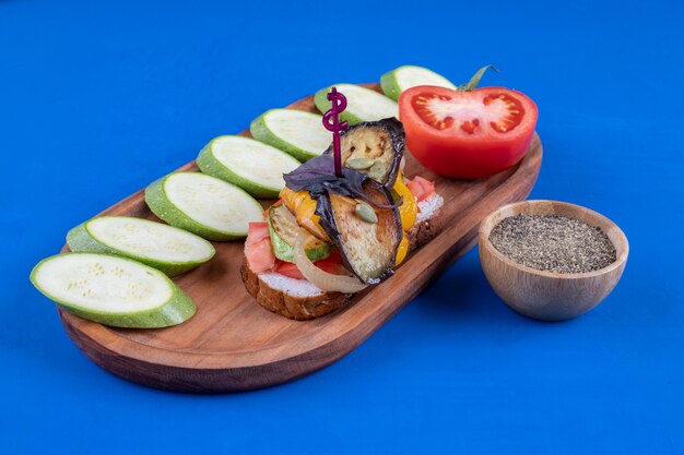 wooden plate of tasty toast with vegetables and zucchinis on blue surface