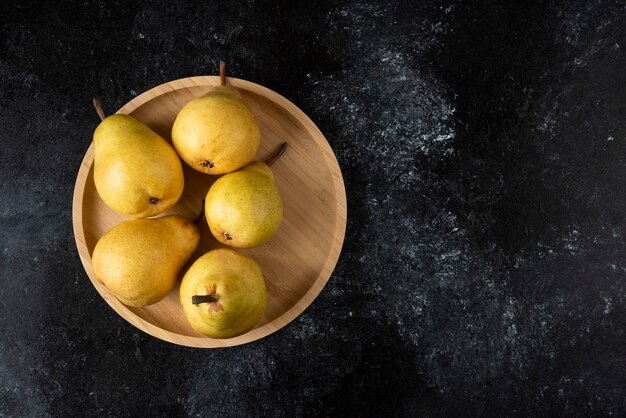 Wooden plate of tasty yellow pears on black surface. 