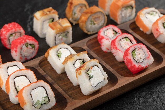 Wooden plate of traditional sushi rolls on black table