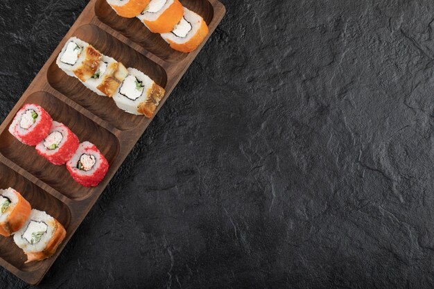 Wooden plate of traditional sushi rolls on black table