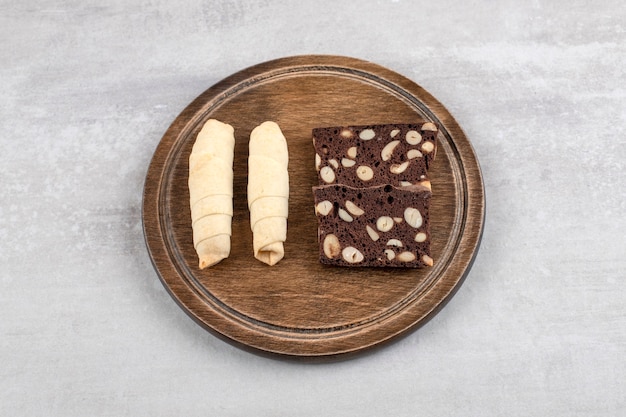 Wooden plate of traditional sweet mutaki and cocoa biscuits on stone table. 