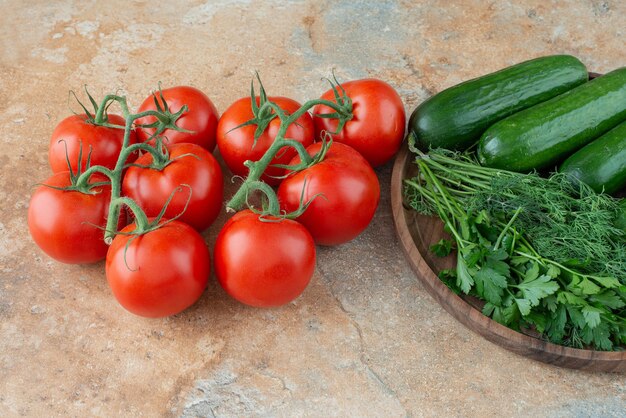 Free photo a wooden plate with cucumbers, greens and tomatoes.