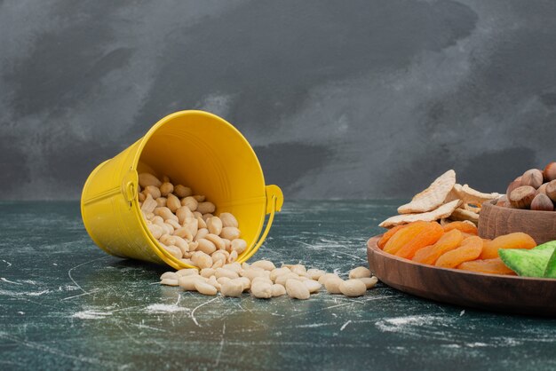 Wooden plate with dried fruits and bucket of nuts .