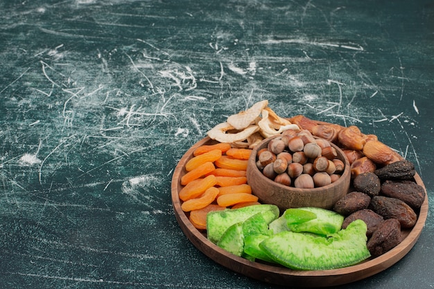 Wooden plate with dried fruits on marble table