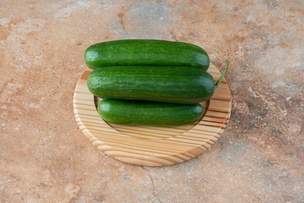 A wooden plate with fresh cucumbers on marble