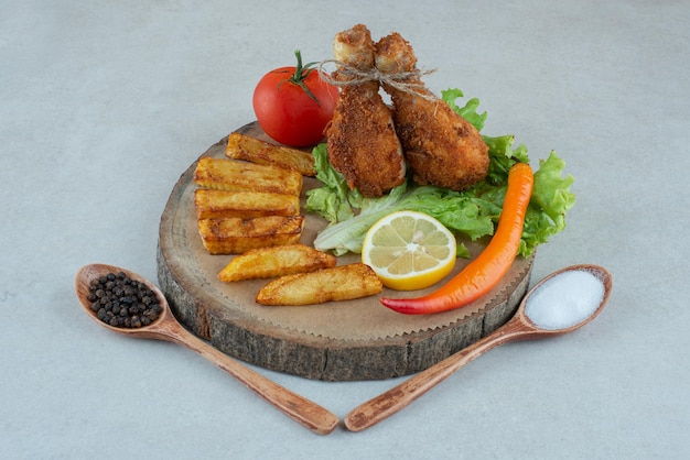A wooden plate with fried cgicken and vegetables on marble table.