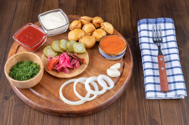 Wooden plate with fried dumplings, ketchup and pickles on wooden surface.