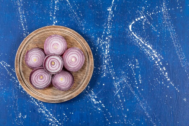 Wooden plate with purple onion rings on marble surface