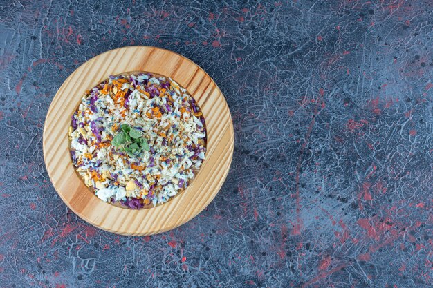 A wooden plate with vegetable salad on marble surface