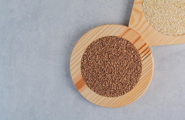 Wooden plates filled with rice and buckwheat on marble surface