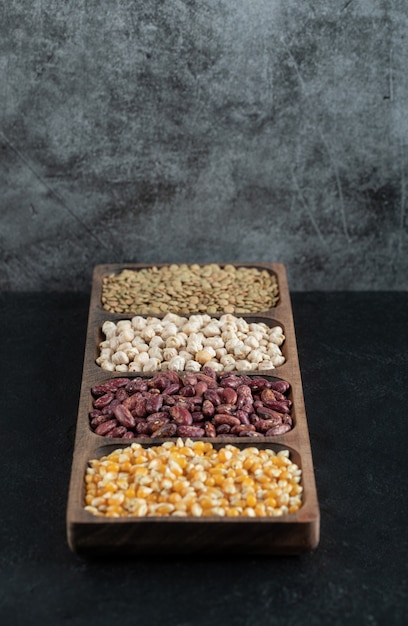 Wooden plates with raw beans and popcorn on black.