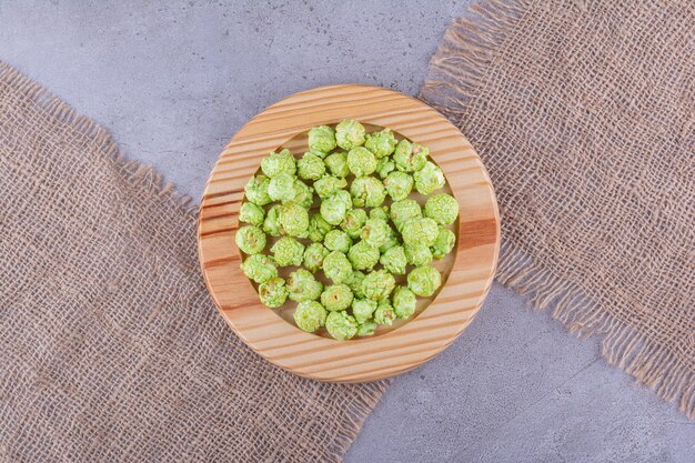 Wooden platter on pieces of cloth, holding a small heap of candied popcorn on marble background. High quality photo