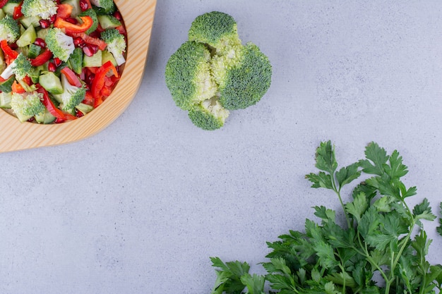 Wooden platter of salad with bundles of broccoli and parsley leaves on marble background. High quality photo