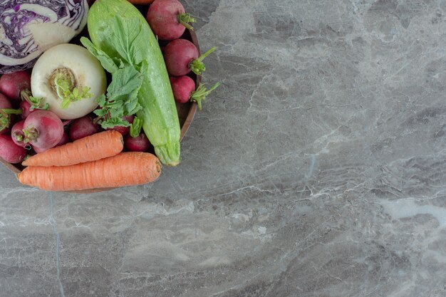 Wooden platter stocked with carrots, squash, turnips, red cabbage and turnip greens on marble.