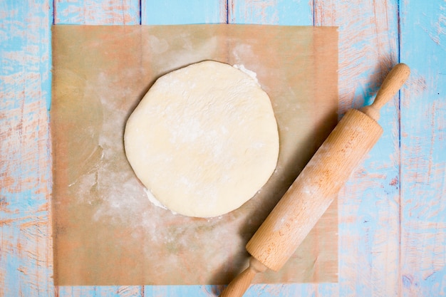 Wooden rolling pin over the flat dough over the parchment paper on wooden table