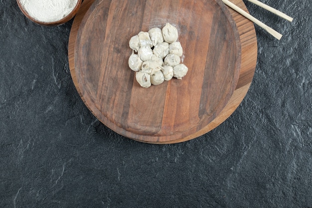 A wooden round board with uncooked dumplings and flour.