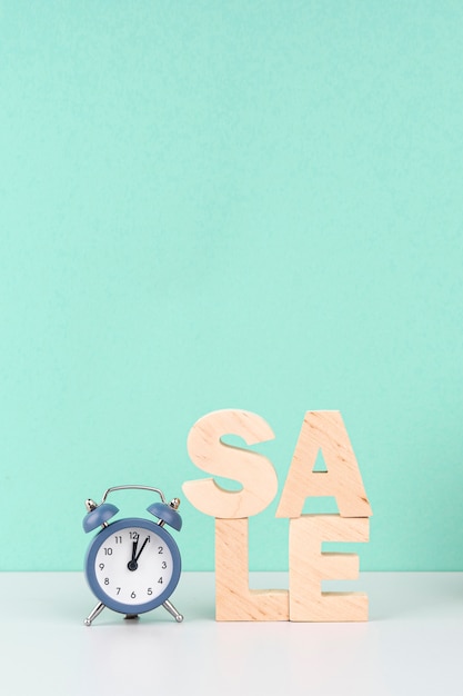 Wooden sale lettering next to clock on blue background