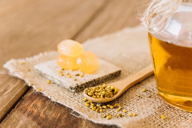 Wooden spoon; bee pollen seeds; candies and jar of honey on sack cloth